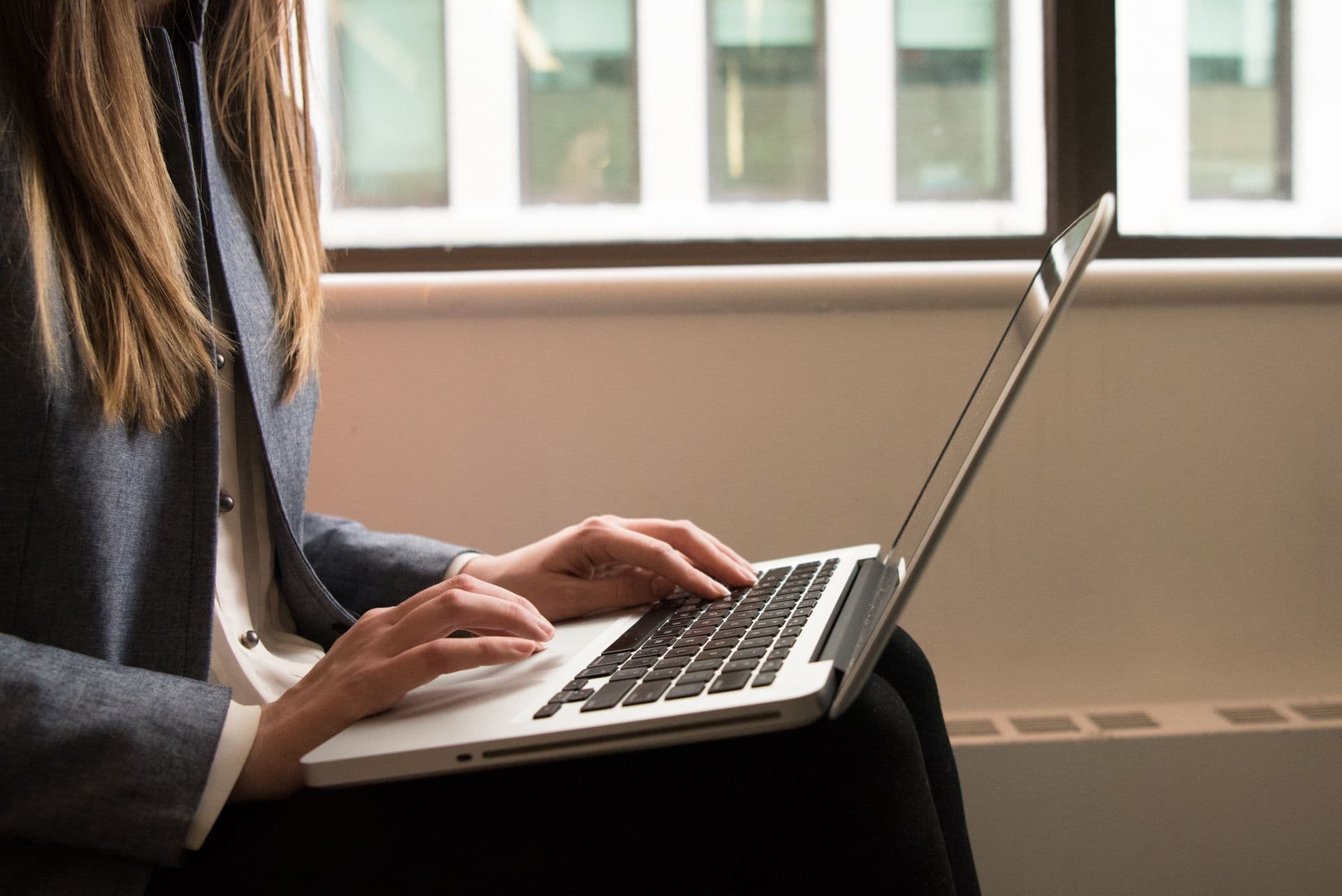 Hands typing on a laptop by a window — illustrative stock photo